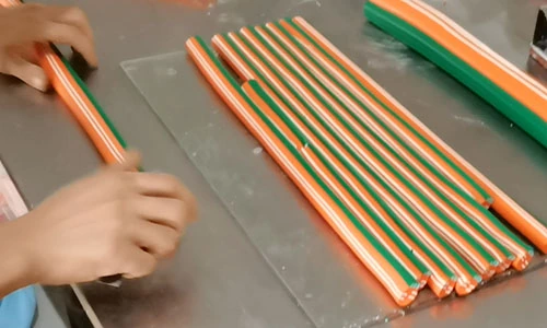Hands arranging orange, green and white patterned clay canes on a worktable