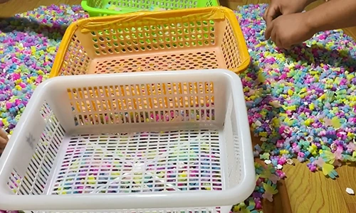 Worker sorting multicoloured resin flatback charms beside collection baskets